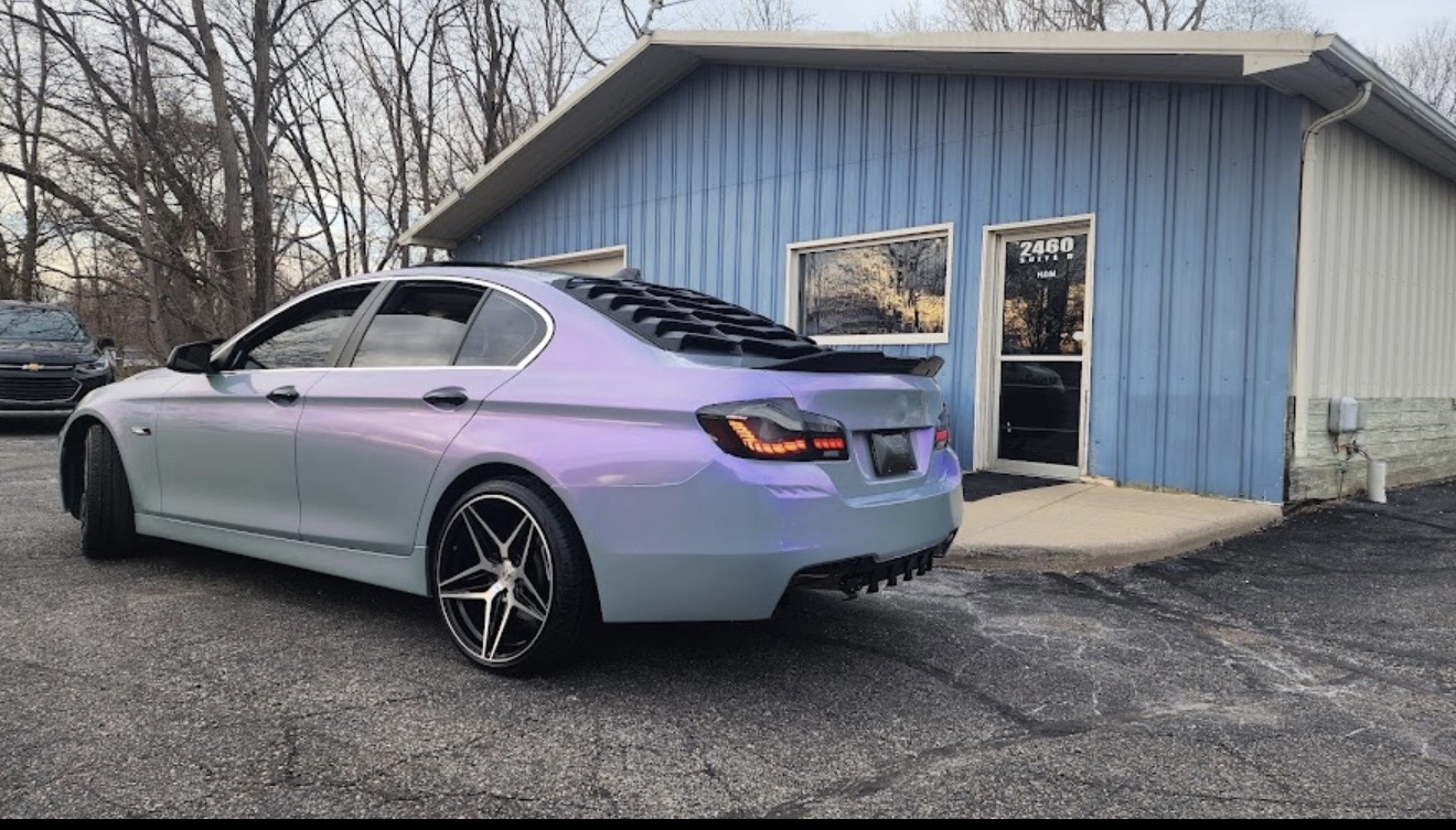 Custom BMW with a color-shift wrap, rear louvers and aftermarket wheels, parked outside the House of Motion shop in Holt, Michigan
